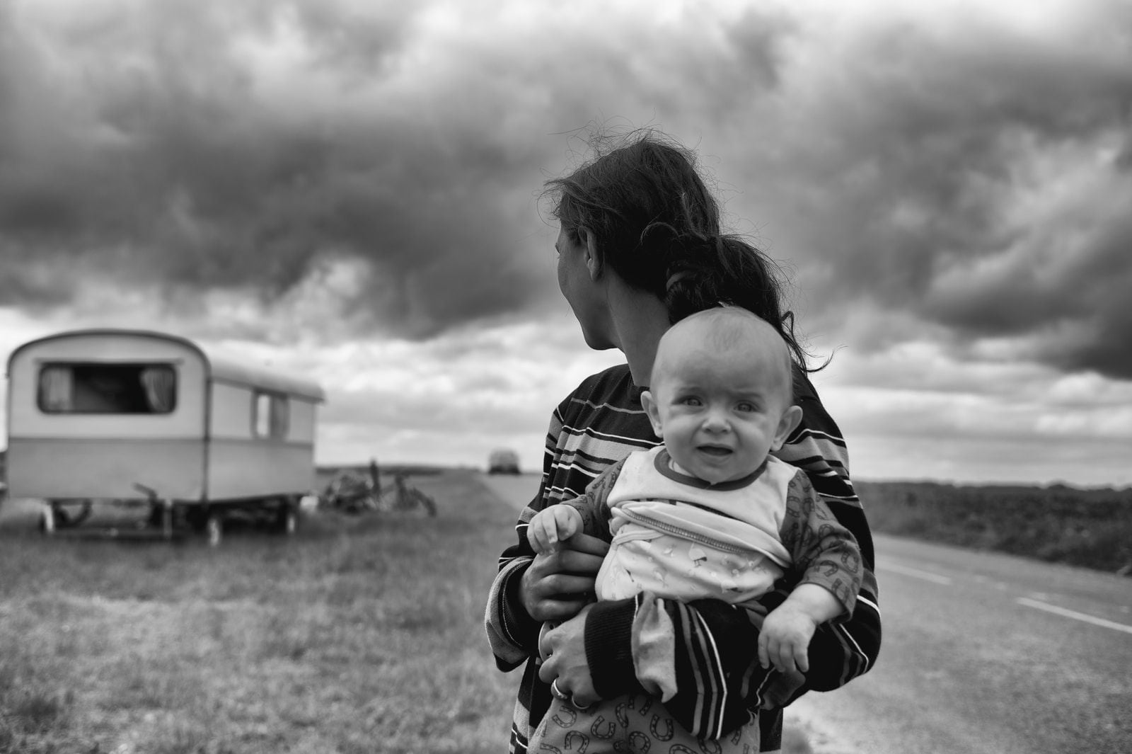 gray scale photography of woman carrying baby looking at camper trailer